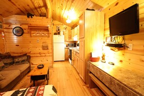Ein Ferienhaus-Innenraum mit Holzausstattung, einem an der Wand montierten Fernseher, einer Küchenzeile und einer Couch.