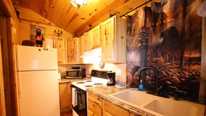 A kitchen with wooden cabinets, a white refrigerator, a stove, a microwave, and a sink. - Bears Den, studio cabin, full kitchen, cover carport, Restmore Inn, Hill City (Hill City)