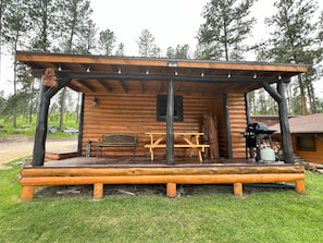 Eine Holzjagdhaus mit überdachter Veranda, einer Bank, einem Tisch und einem Grill.