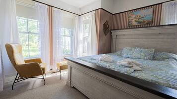 Ein Schlafzimmer mit einem großen Bett, einem Sessel, einem kleinen Tisch und einem Gemälde an der Wand.