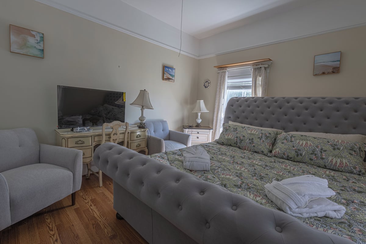 A bedroom with a large bed, a sofa, a TV, a desk, and a window with curtains.