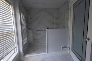 Suihkukaappi, jossa on lasiovi, valkoisilla laatoilla päällystetty lattia ja ovi, jossa on kahva.