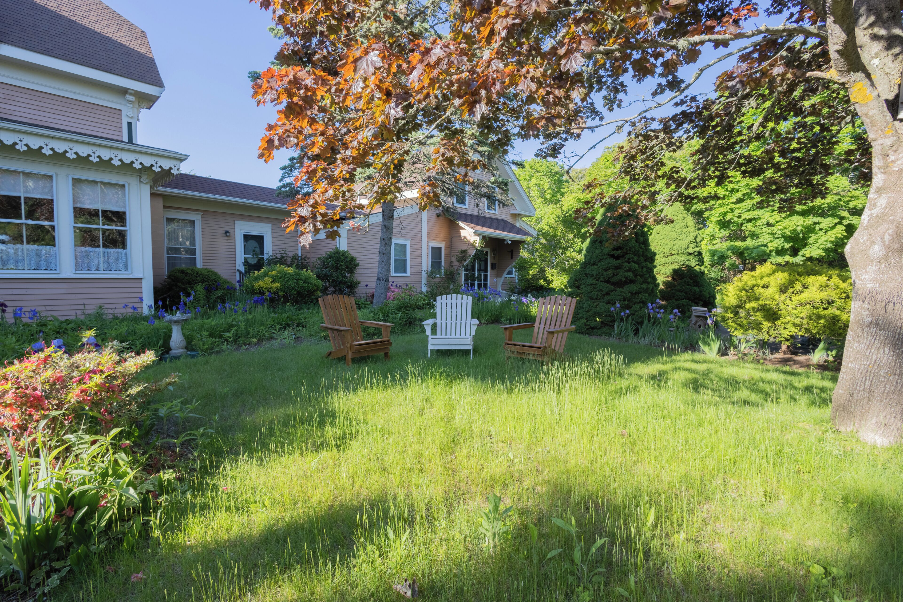 Une maison avec un porche à l’avant, une pelouse et deux fauteuils Adirondack.