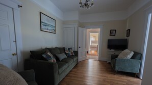A living room with a sofa, a chair, a television, and a hallway leading to another room. - The Villa Callo Inn (West Harwich)