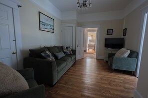 A living room with a sofa, a chair, a television, and a hallway leading to another room.