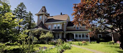 A large, multi-story house with a well-maintained garden and a clear sky.
