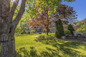 A residential area with a well-maintained lawn, a large tree with autumn leaves, and a house with a porch.