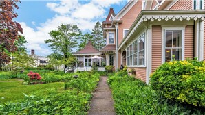 A traditional house with a garden pathway leading to the entrance, surrounded by lush greenery and a white picket fence. - The Villa Callo Inn (West Harwich)