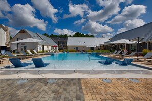 Une piscine avec des chaises longues, un espace abrité et un bâtiment doté d’un toit en pente.