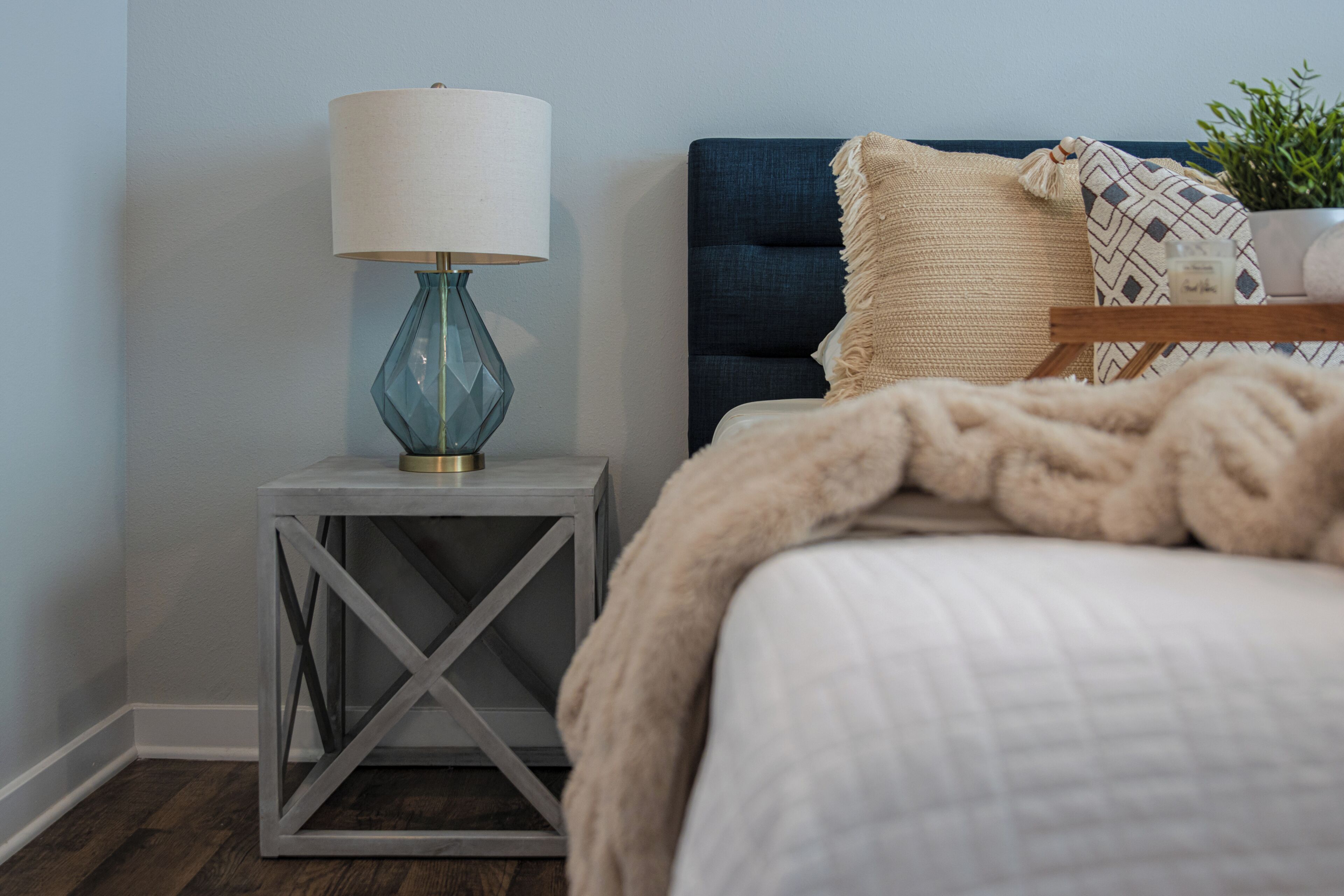 A neatly arranged bedroom with a bed, a bedside table with a lamp, and a small plant.