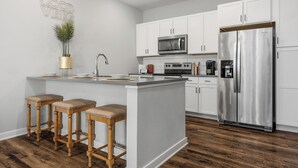 A modern kitchen with white cabinets, a stainless steel refrigerator, a microwave, and wooden stools. - Cozy 1-bedroom in the heart of Madison (Madison)