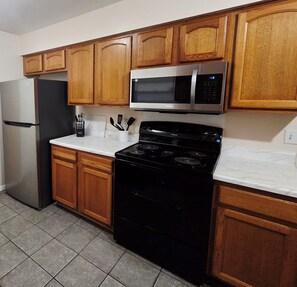 A kitchen with wooden cabinets, a stainless steel refrigerator, a microwave, and a black stove.