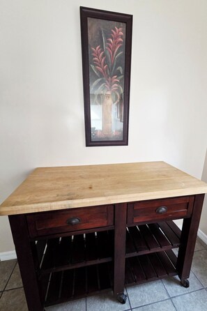 Una mesa de madera con cajones y un estante, ubicada frente a una pared con un cuadro enmarcado encima.