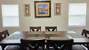 Un coin repas avec une table en bois, six chaises et trois tableaux encadrés accrochés au mur.
