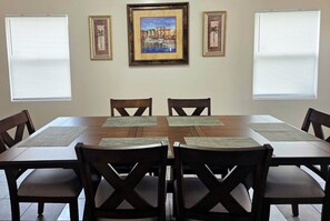 A dining area with a wooden table, six chairs, and three framed pictures on the wall.
