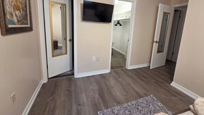 Un couloir doté d’un plancher en bois, d’un téléviseur à écran plat fixé au mur et d’une porte donnant sur un placard.