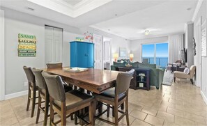 A dining area with a wooden table and chairs, a blue cabinet, and a wall with a beach-themed sign. - Ocean Ritz 2001! Gulf Views, 4BR Penthouse Beachfront Escape (Panama City Beach)
