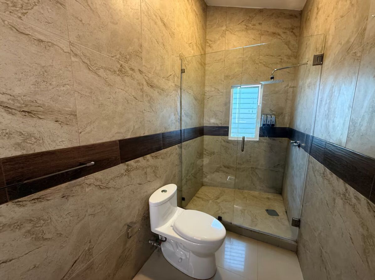 A bathroom with a toilet, a shower enclosure, and a marble wall.