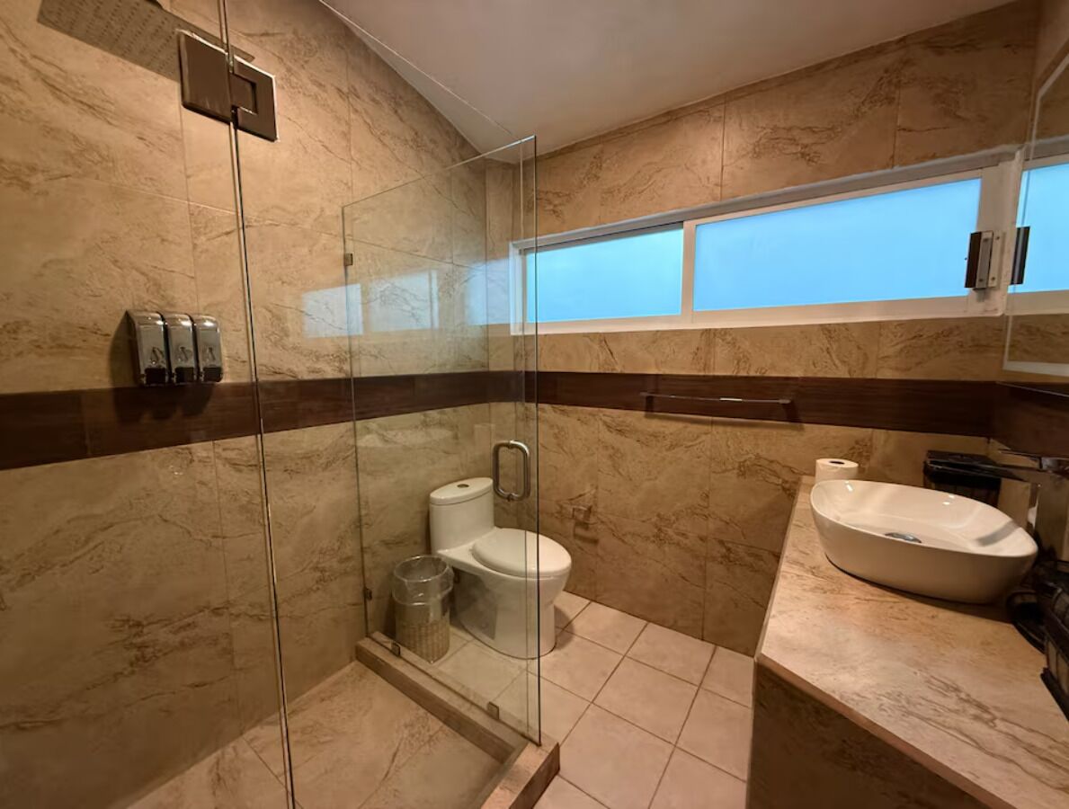 A bathroom with a glass-enclosed shower, a toilet, a sink, and a window above the sink.
