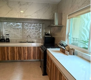 Eine moderne Küche mit Marmor-Spritzschutz, Holzschränken, einem eingebauten Herd und einem Fenster mit Ausblick.