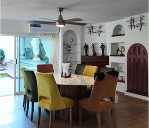 Ein Essbereich mit einem Marmortisch, gelb-grünen Stühlen, einem Deckenventilator und Dekorationen auf Regalen.