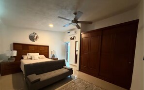 Ein Schlafzimmer mit einem Bett, Nachttischen, einem Deckenventilator, einem großen Kleiderschrank und einer Tür zu einem Badezimmer.