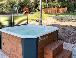 A hot tub with a wooden exterior and steps leading up to it, set in a backyard with a fence and trees in the background. - Comfortable Holiday Villa, Sauna, Jacuzzi (Brzeznica)
