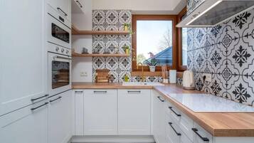 A modern kitchen with white cabinetry, a built-in oven, a window with a view, and patterned backsplash tiles.