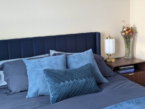 A neatly made bed with a dark headboard, a bedside table with a lamp, and a vase with flowers.