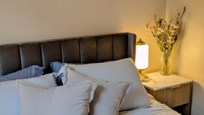 Un lit bien fait, avec des oreillers, une lampe de chevet et un vase de fleurs posé sur une table de chevet.