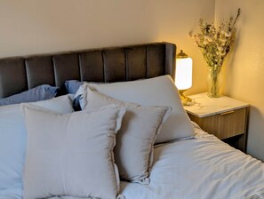 A neatly made bed with pillows, a bedside lamp, and a vase with flowers on a nightstand. - Historic Main St w/ Lake View | The Flatwater Loft (Ashland)