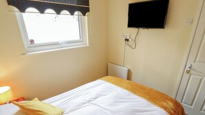 Une chambre à coucher avec un lit, une fenêtre, un téléviseur fixé au mur et une porte.