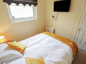 Ein Schlafzimmer mit einem Bett, einem Fenster, einem an der Wand befestigten Fernseher und einer Tür.