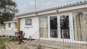 Une maison mobile de plain-pied dotée d’un patio, d’une petite table et de quelques chaises, ainsi que d’un ensemble de marches menant à l’entrée.