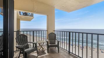 A balcony with two Adirondack chairs, a small table, and a view of the beach and ocean.