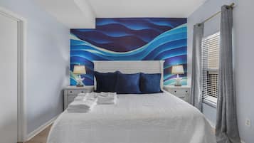 A bedroom with a bed, white headboard, two bedside tables with lamps, a window with curtains, and a wall mural.