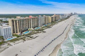 Ein Strandhotel mit mehreren Gebäuden, einem Sandstrand und einer Reihe von Sonnenschirmen.