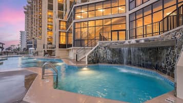 A hotel with a pool, a waterfall feature, and multiple balconies with lights.
