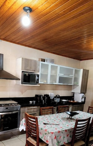 Cozinha com teto de madeira, armários brancos, fogão e mesa de jantar com cadeiras.