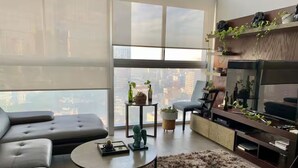 Una sala moderna con sofá, mesa de centro, televisor y vista a la ciudad.