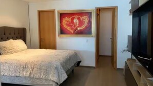 Un dormitorio con cama, televisor, un cuadro y una puerta.