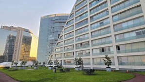 Un hotel moderno con varios pisos, grandes ventanales y un espacio exterior cuidado con mobiliario y plantas.