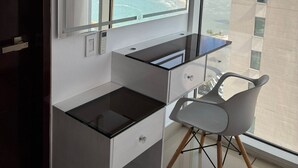 Quarto moderno com uma grande janela, uma escrivaninha, uma cadeira e vista para o oceano e a cidade.