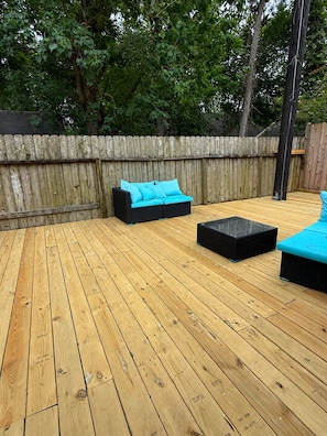 A wooden deck with outdoor furniture, a wooden fence, and trees in the background.
