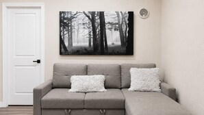 A grey sectional sofa with two white patterned cushions, a white door, and a forest-themed artwork on the wall. - Private Guest House Free Parking 20min to IAH Airport (Houston)