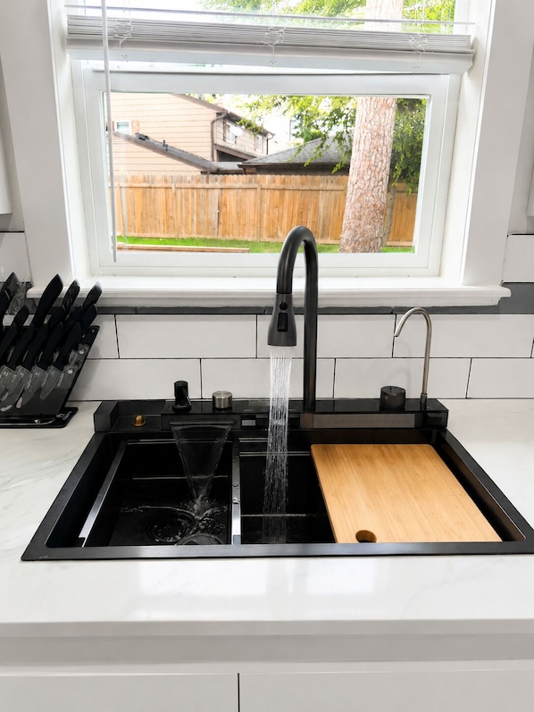 A kitchen with a black faucet, a wooden cutting board, and a knife block.