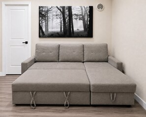 A sectional sofa with a patterned fabric, a door, and a wall-mounted artwork of a forest scene.