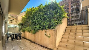A courtyard with a tiled floor, a table with chairs, a staircase, and a wall covered with ivy. - Le Nid Mentonnais - À moins de 100 m de la plage (Menton)