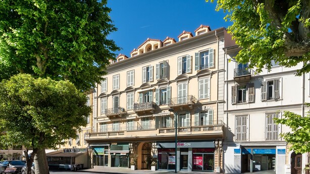 A multi-story building with a central entrance, storefronts on the ground floor, and balconies on the upper floors. - Le Nid Mentonnais - À moins de 100 m de la plage (Menton)