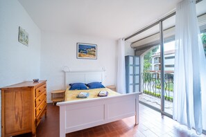 A bedroom with a bed, wooden dresser, and a view through a large window. - El Tiburon N°17 - À 250 m de la plage (Argeles-sur-Mer)